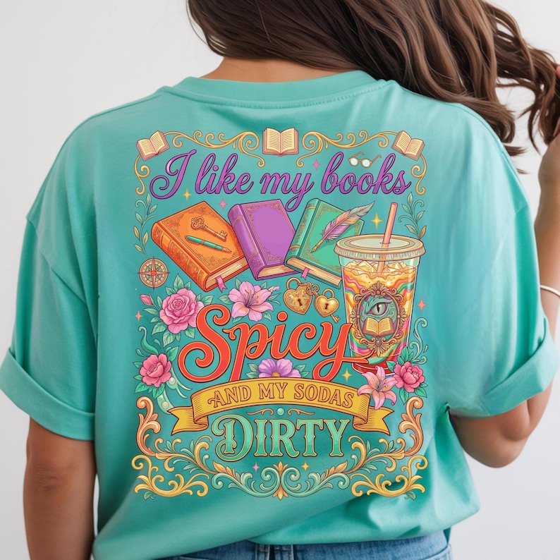 May include: Teal t-shirt with a colorful graphic that reads "I like my books Spicy and my sodas Dirty." The design includes books, flowers, and a drink with a straw. The shirt has short sleeves.