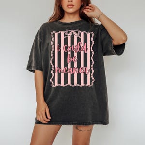 May include: Dark gray oversized t-shirt with a pink and white striped design. The design features the text "i could be meaner" in a pink script font, framed by a decorative border and a bow.