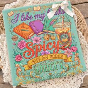 May include: A teal graphic tee with the text "I like my books spicy and my sodas dirty." The design features colorful illustrations of books, flowers, and a soda cup. A white bow is attached to the top.