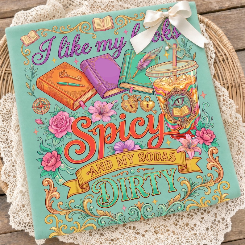 May include: A teal graphic tee with the text "I like my books spicy and my sodas dirty." The design features colorful illustrations of books, flowers, and a soda cup. A white bow is attached to the top.
