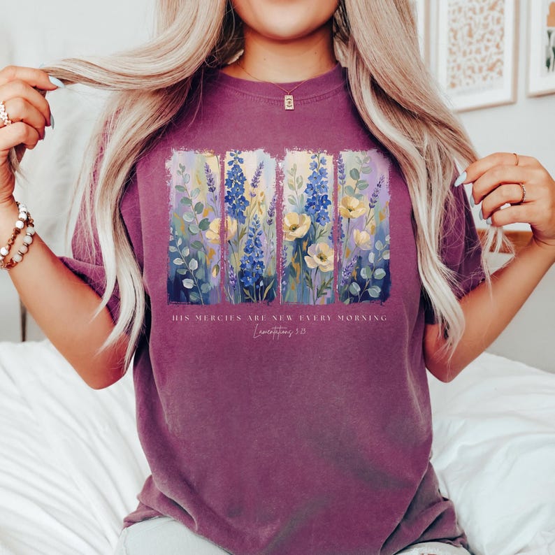 Puede incluir: Camiseta granate con un dise&ntilde;o floral con flores azules, amarillas y moradas. El texto "HIS MERCIES ARE NEW EVERY MORNING Lamentations 3:23" est&aacute; impreso debajo del dise&ntilde;o floral.