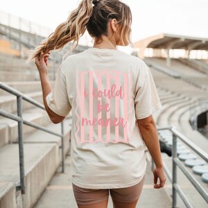 May include: Cream-colored t-shirt with the phrase "I could be meaner" in pink script within a pink striped frame. The shirt is a casual style, suitable for everyday wear.