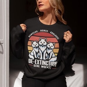 Op de afbeelding: Zwart sweatshirt met een retro-grafische afbeelding van drie witte direwolves met de tekst "Romulus - Remus - Khaleesi De-Extinction Dire Wolves".