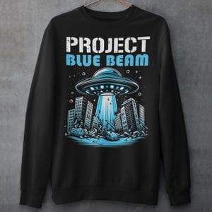 This bold and striking sweatshirt features a dramatic scene of a UFO hovering menacingly above a futuristic city, casting a glowing beam of light that tears through skyscrapers, causing chaos and destruction below. The detailed artwork captures the intensity of the moment, with crumbling buildings giving the design an apocalyptic feel. Above the imagery, the text "PROJECT BLUE BEAM" is emblazoned in bold, futuristic typography, adding a mysterious and conspiracy-driven edge to the design.