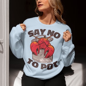 Może przedstawiać: Jasno błękitna bluza z napisem "Say No To Pot" i kreskówkowym homarem w garnku.