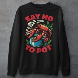 May include: Black sweatshirt featuring a red and white graphic of a lobster holding a cigarette and sitting in a blue pot. The text "SAY NO TO POT" is printed in red.