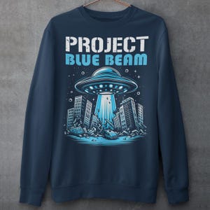 This bold and striking sweatshirt features a dramatic scene of a UFO hovering menacingly above a futuristic city, casting a glowing beam of light that tears through skyscrapers, causing chaos and destruction below. The detailed artwork captures the intensity of the moment, with crumbling buildings giving the design an apocalyptic feel. Above the imagery, the text "PROJECT BLUE BEAM" is emblazoned in bold, futuristic typography, adding a mysterious and conspiracy-driven edge to the design.