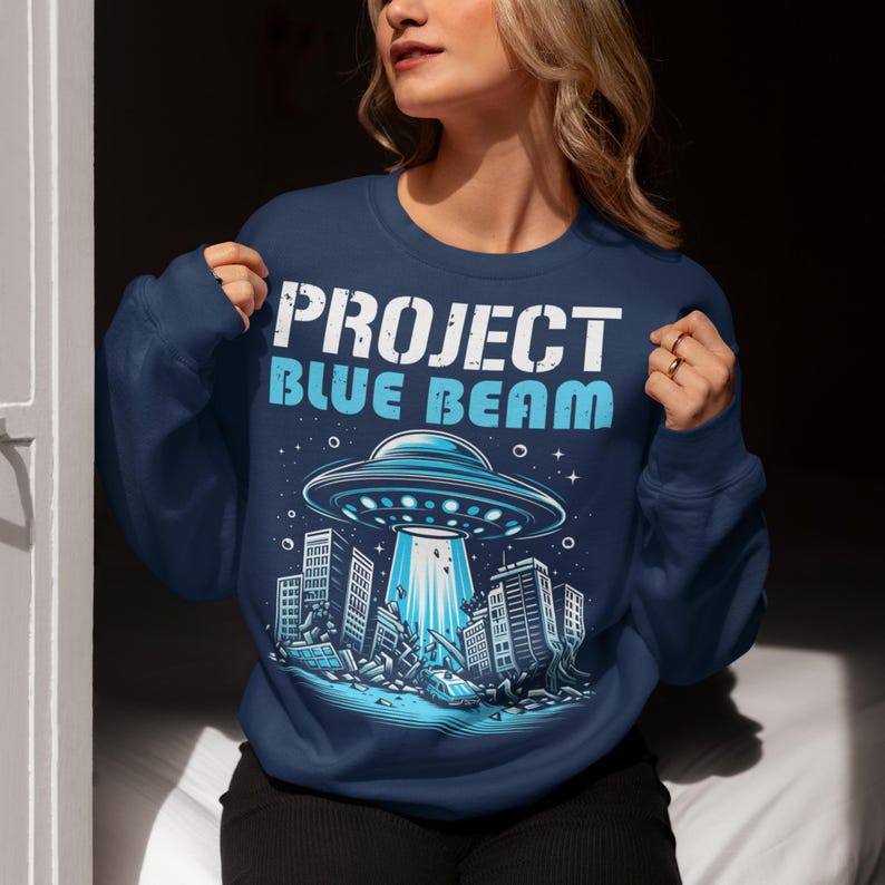 This bold and striking sweatshirt features a dramatic scene of a UFO hovering menacingly above a futuristic city, casting a glowing beam of light that tears through skyscrapers, causing chaos and destruction below. The detailed artwork captures the intensity of the moment, with crumbling buildings giving the design an apocalyptic feel. Above the imagery, the text "PROJECT BLUE BEAM" is emblazoned in bold, futuristic typography, adding a mysterious and conspiracy-driven edge to the design.