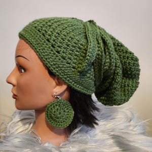 May include: A green crocheted beanie with a slouchy fit. The beanie is worn on a mannequin with green crocheted earrings.