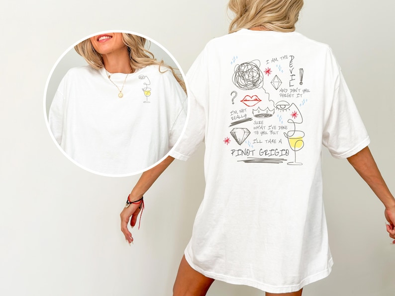 May include: White t-shirt with a minimalist wine glass design on the front and a playful illustration on the back. The back graphic includes the text "I AM THE DEVIL" and "I'LL TAKE A PINOT GRIGIO."