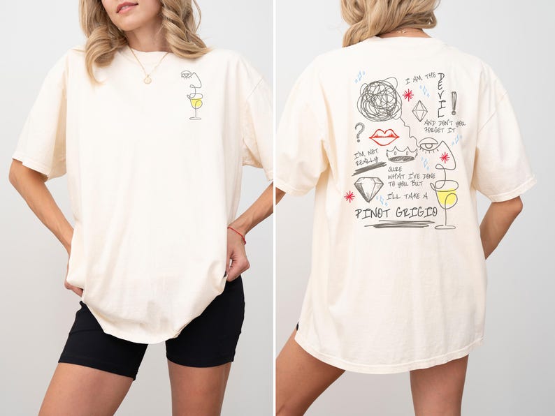 May include: Cream-colored oversized t-shirt with a line drawing of a face and a wine glass on the front. The back features a sketched design with text including "I'll take a Pinot Grigio."