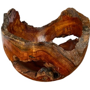 May include: A rustic wooden bowl with a natural, irregular shape and a rich brown colour. The bowl has a unique, organic design with a hole on one side, making it a decorative and functional piece.