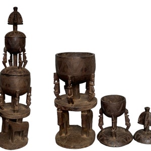 May include: Four intricately carved wooden bowls with a tiered design. The bowls are dark brown and feature a geometric pattern. The largest bowl is stacked on top of two smaller bowls, and the smallest bowl is separate. The bowls are all supported by small figures carved into the wood.
