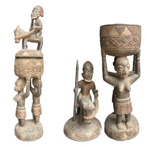 Könnte beinhalten: Drei Holzskulpturen von Menschen, die jeweils ein anderes Objekt halten. Die erste Skulptur zeigt eine Person, die auf einem Pferd reitet, die zweite eine Person, die eine Schüssel hält, und die dritte eine Person, die einen Korb hält. Die Skulpturen sind alle im traditionellen afrikanischen Stil geschnitzt.