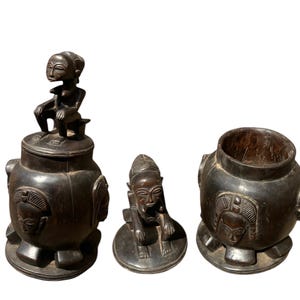 May include: Three intricately carved wooden containers with human figures. The containers are dark brown and have a smooth, polished finish. The figures are carved in a stylized, tribal style and have expressive faces.