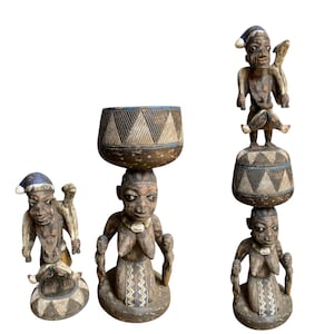 Könnte beinhalten: Drei geschnitzte Holzskulpturen von Figuren mit gemusterten Details. Die Figuren haben eine dunkelbraune Oberfläche mit helleren Akzenten. Eine Figur hält eine Schüssel auf dem Kopf, während andere Figuren auf ihren Köpfen haben. Die Skulpturen haben eine Stammeskunst-Ästhetik.