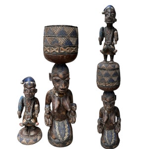 Puede incluir: Tres esculturas de madera de personas pintadas en azul y marrón. Las esculturas están talladas en un estilo tradicional y tienen un aire tribal. Las esculturas están de pie sobre un fondo blanco.