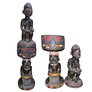 Puede incluir: Cuatro esculturas de madera oscura de figuras humanas. Las esculturas tienen patrones geométricos rojos, azules y amarillos. Las figuras están sentadas o de pie, con rasgos faciales tallados. Probablemente se trate de arte africano.