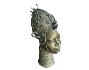 May include: A bronze sculpture of a person's head wearing a crown with intricate details. The sculpture is a traditional African art piece.