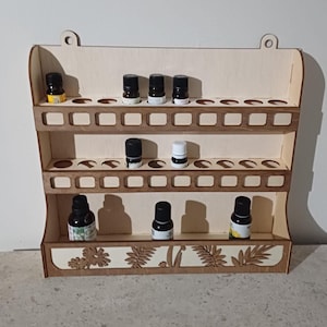 Peut inclure: Un porte-bouteilles d'huiles essentielles en bois avec deux étagères et une bordure inférieure décorative. Le porte-bouteilles a 24 emplacements pour bouteilles et est rempli de diverses bouteilles d'huiles essentielles.