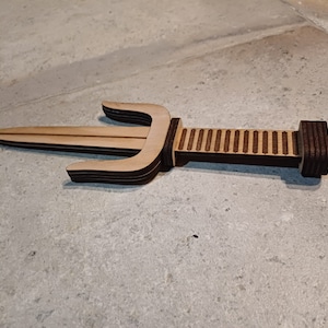 May include: A wooden sai, a traditional Okinawan weapon, with a brown and light brown color scheme. The sai has a double-pronged blade and a handle with a striped pattern.