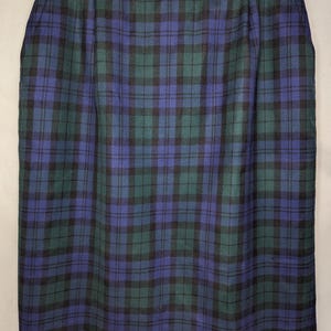 May include: A knee-length skirt with a classic plaid pattern in shades of blue, green, and black. The skirt is hanging on a hanger, showcasing its tailored design and the fabric's texture. The plaid pattern is evenly distributed across the skirt.