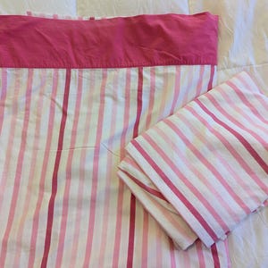 May include: A pink and white striped bed sheet set. The set includes a flat sheet with a solid pink top border, a fitted sheet, and a folded pillowcase. The sheets have vertical stripes in varying shades of pink and white.