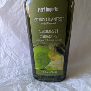 May include: A clear plastic bottle filled with dark green reed diffuser oil. The label reads Pier 1 imports, CITRUS CILANTRO reed diffuser oil, and AGRUMES ET CORIANDRE, with images of a lime and lemon. The bottle contains 16 fl oz of liquid.