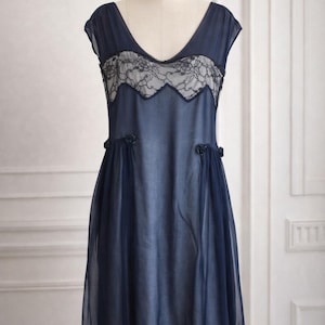 Può includere: Abito blu navy in stile vintage con scollo a V e maniche a cappuccio. L'abito presenta un delicato pannello in pizzo sul corpetto e rifiniture in pizzo sull'orlo. Piccoli accenti floreali adornano la vita.