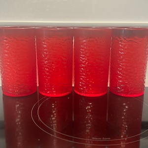 May include: Four red glass tumblers with a textured surface sit on a black electric stovetop with a white control panel above. The control panel has buttons for "Bake", "Broil", "Keep Warm", "Precise Clean", "Warm Zone On", and "Warm Zone Off".