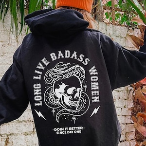 May include: Black hooded sweatshirt with a white graphic print of a skull with a snake wrapped around it. The text "Long Live Badass Women" is printed around the skull. The text "Doin' it Better Since Day One" is printed below the skull.