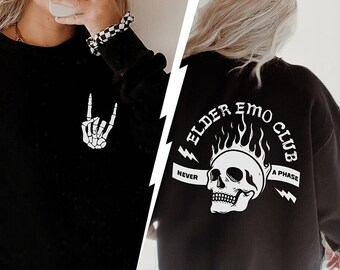 May include: A black sweatshirt featuring a white skeleton hand making a rock-and-roll gesture on the front. The back displays a white graphic of a flaming skull with the text ELDER EMO CLUB and NEVER A PHASE printed in a bold, distressed font.