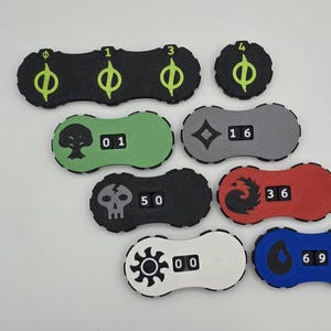 May include: Nine different colored and shaped tokens with various symbols and numbers. The tokens are made of foam and have a textured surface. The symbols include a skull, a tree, a diamond, a phoenix, a sun, and a teardrop. The numbers range from 00 to 69.