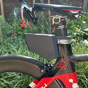 Könnte beinhalten: Ein schwarzes und rotes Rennrad mit einer schwarzen Aufbewahrungsbox am Rahmen. Das Fahrrad hat einen schwarzen Sattel und einen rot-schwarzen Helm. Der Rahmen hat ein rotes Blumendesign.