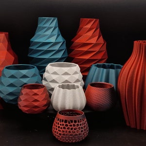 Könnte beinhalten: Eine Sammlung von 10 geometrischen Vasen in verschiedenen Rot-, Blau- und Grautönen. Die Vasen sind aus einem strukturierten Material gefertigt und haben eine Vielzahl von Formen und Größen.