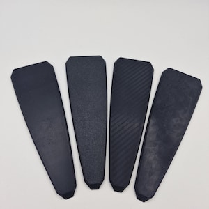 May include: Four black rectangular pieces of material with different textures. The textures include a smooth, a textured, a carbon fiber, and a marbled pattern.