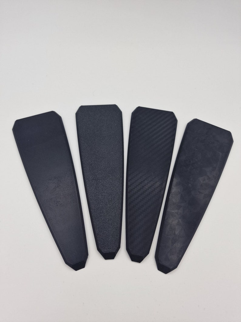 May include: Four black rectangular pieces of material with different textures. The textures include a smooth, a textured, a carbon fiber, and a marbled pattern.