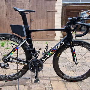May include: A black Specialized S-Works road bike with a black and white Roval wheelset. The bike has a black frame, black handlebars, and a black seat. The bike is on a stand and has a black water bottle cage.