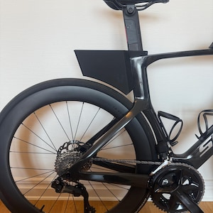 May include: Black road bike with a sleek design. Features include a black seat, wheels, and frame. The bike has a disc brake system and a water bottle cage. The tires have a diameter of approximately 28 inches.