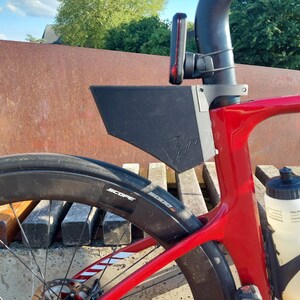 Puede incluir: Una bicicleta roja y negra con una jaula de botella de agua negra y una botella de agua negra. La bicicleta tiene un guardabarros trasero negro y una tija de sillín negra. La bicicleta está aparcada en un banco de madera.