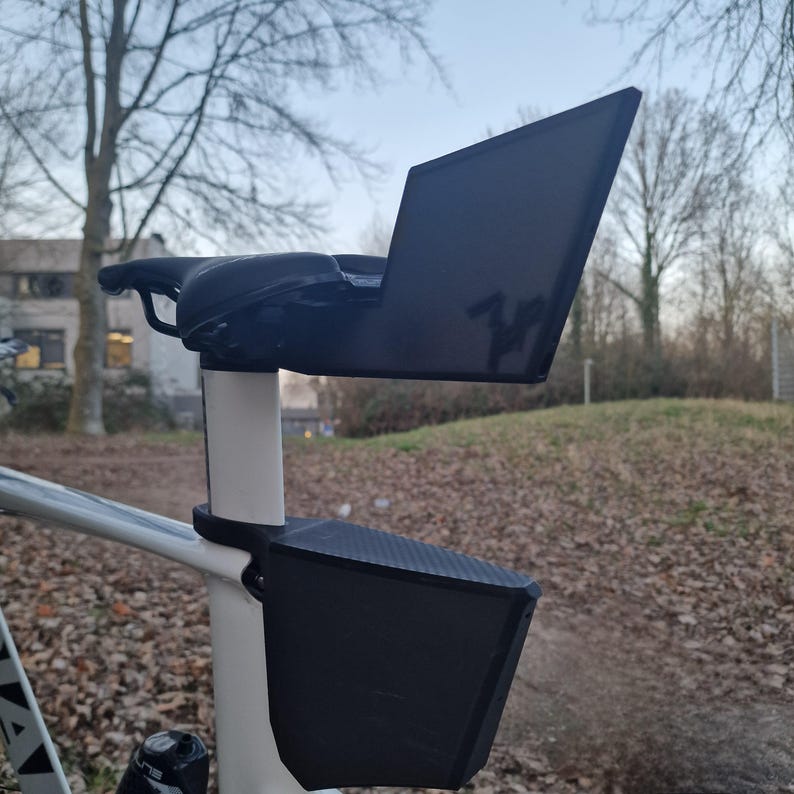 May include: A black bicycle saddle bag and a matching black rear mudguard mounted to the seat post of a white bicycle. The mudguard extends upward behind the saddle, while the storage bag is secured directly below it on the frame post.