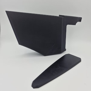 May include: A black plastic 3D printed object with a handle and a separate black plastic piece. The object has a logo on the side.