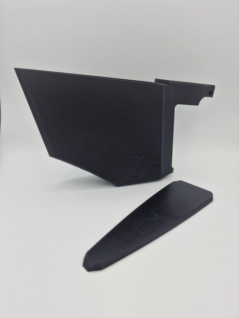 May include: A black plastic 3D printed object with a handle and a separate black plastic piece. The object has a logo on the side.