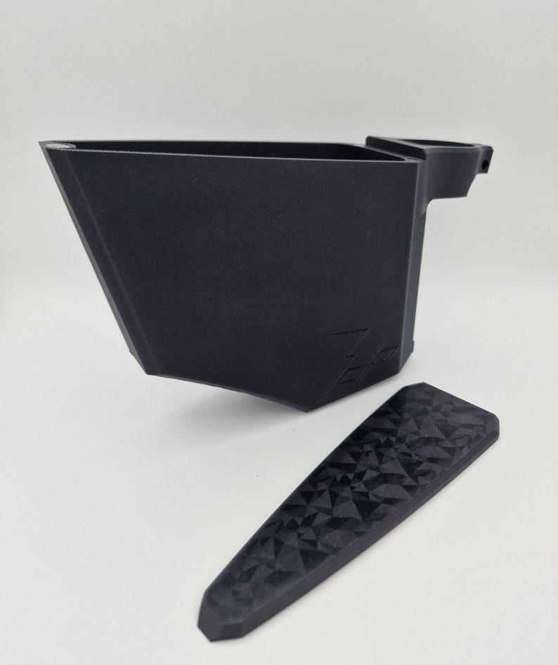 May include: A black 3D printed object with a textured surface and a handle. The object is in two pieces, one is a container and the other is a lid. The lid has a geometric pattern.