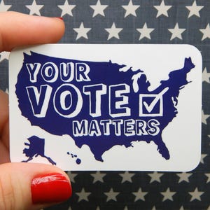May include: A white rectangular sticker with a blue outline of the United States. The words "YOUR VOTE MATTERS" are in white, with a checkmark inside a box. The background is a blue fabric with white stars.