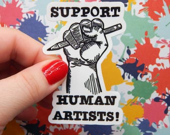 May include: A white sticker with black text and a black and white illustration of a clenched fist holding a pencil. The text reads "SUPPORT HUMAN ARTISTS!" The background is a colorful splatter design.