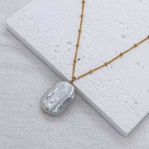May include: A gold chain necklace with a large, white baroque pearl pendant.