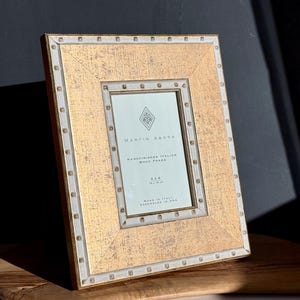May include: A rectangular gold-toned picture frame with a textured surface and white trim. The frame has a central opening with a white border. The text "MARTIN ABORN" and "HAND FINISHED ITALIAN WOOD FRAME" are visible. The frame is 4x6 inches.