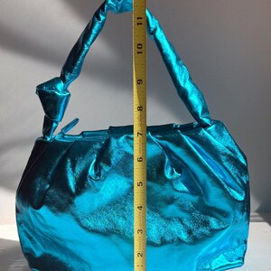 May include: A turquoise handbag with a metallic sheen. The bag has a gathered design and a twisted handle. The height of the bag is approximately 10 inches.