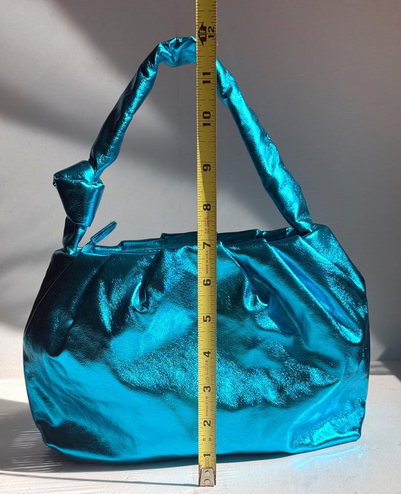 May include: A turquoise handbag with a metallic sheen. The bag has a gathered design and a twisted handle. The height of the bag is approximately 10 inches.
